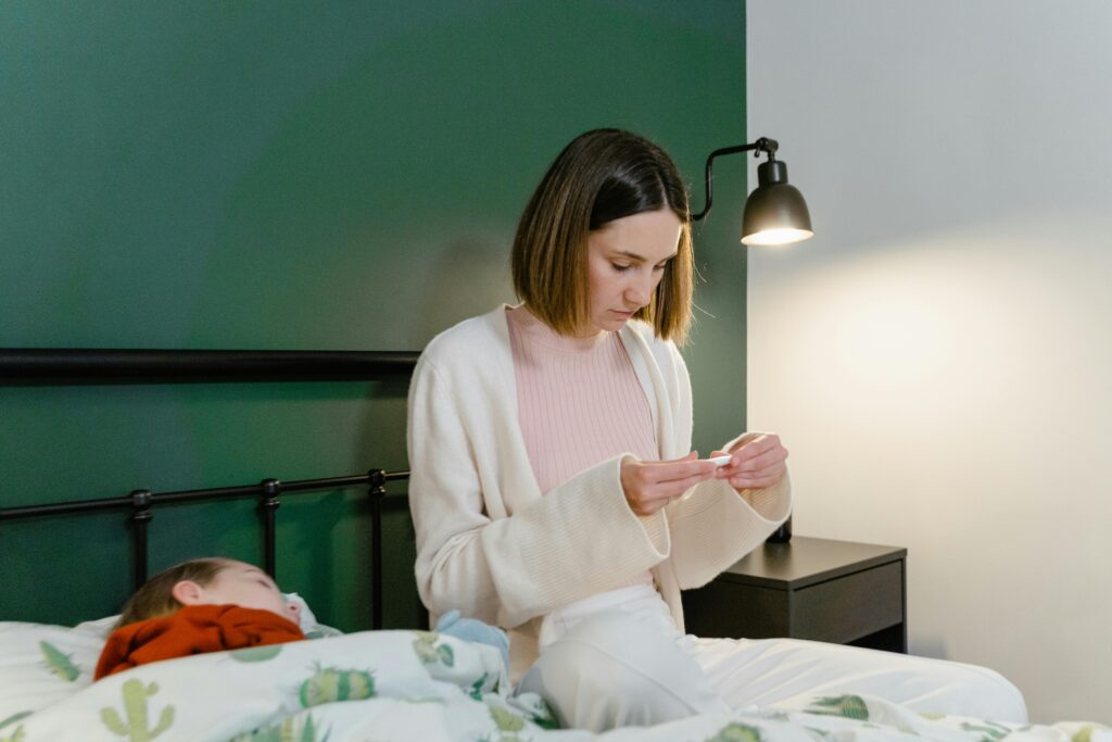 A concerned mother checks her sick child's temperature in a bedroom setting.