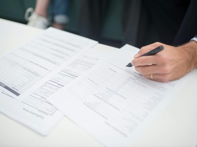 Close-up of a hand signing insurance documents in an office setting.